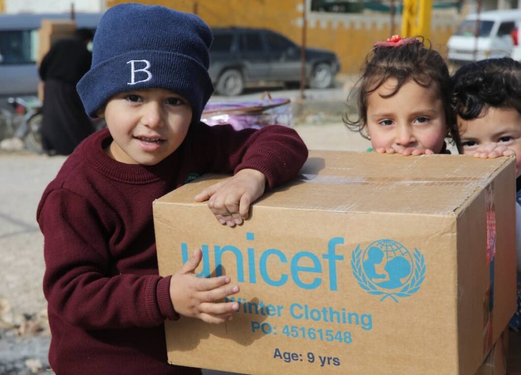 Siromašna djeca drže kutiju pomoći na kojoj piše "unicef winter clothing".